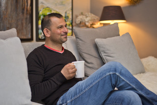 Gentleman client sat on the sofa and smiling whilst holding a mug of tea inside the therapy room.
