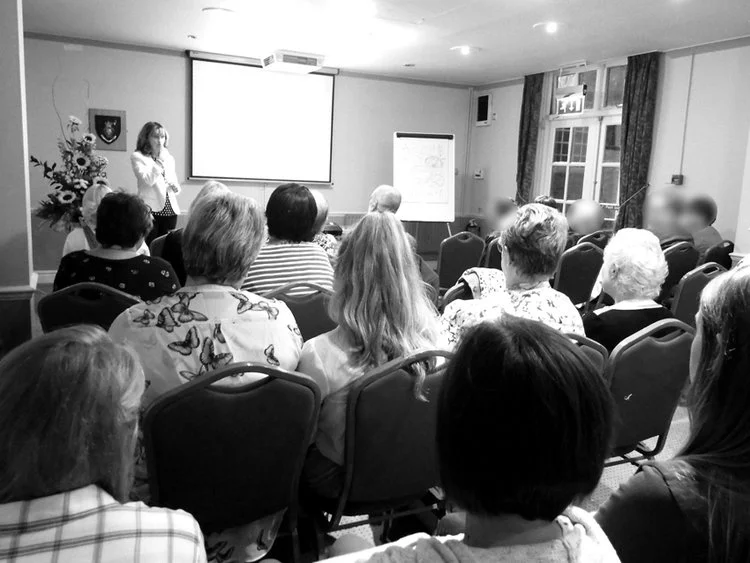 Elva Carter speaking at her corporate counselling event and explaining information to an audience on two whiteboards.